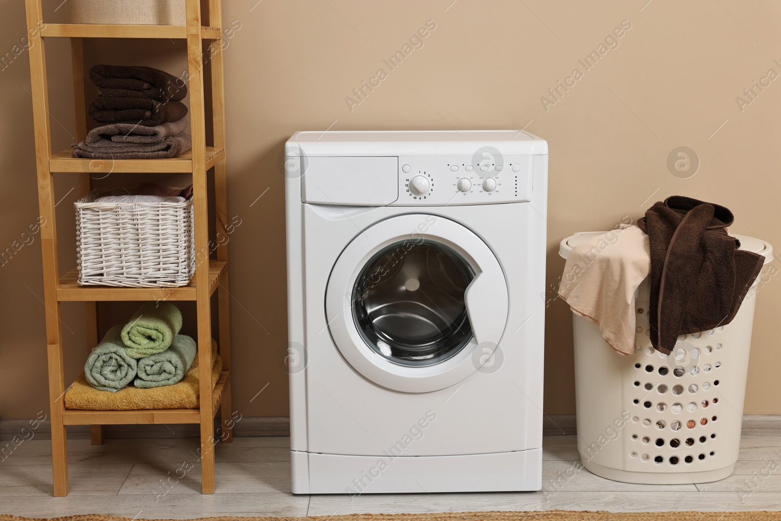 Photo of Washing machine, basket and shelving unit near beige wall indoors