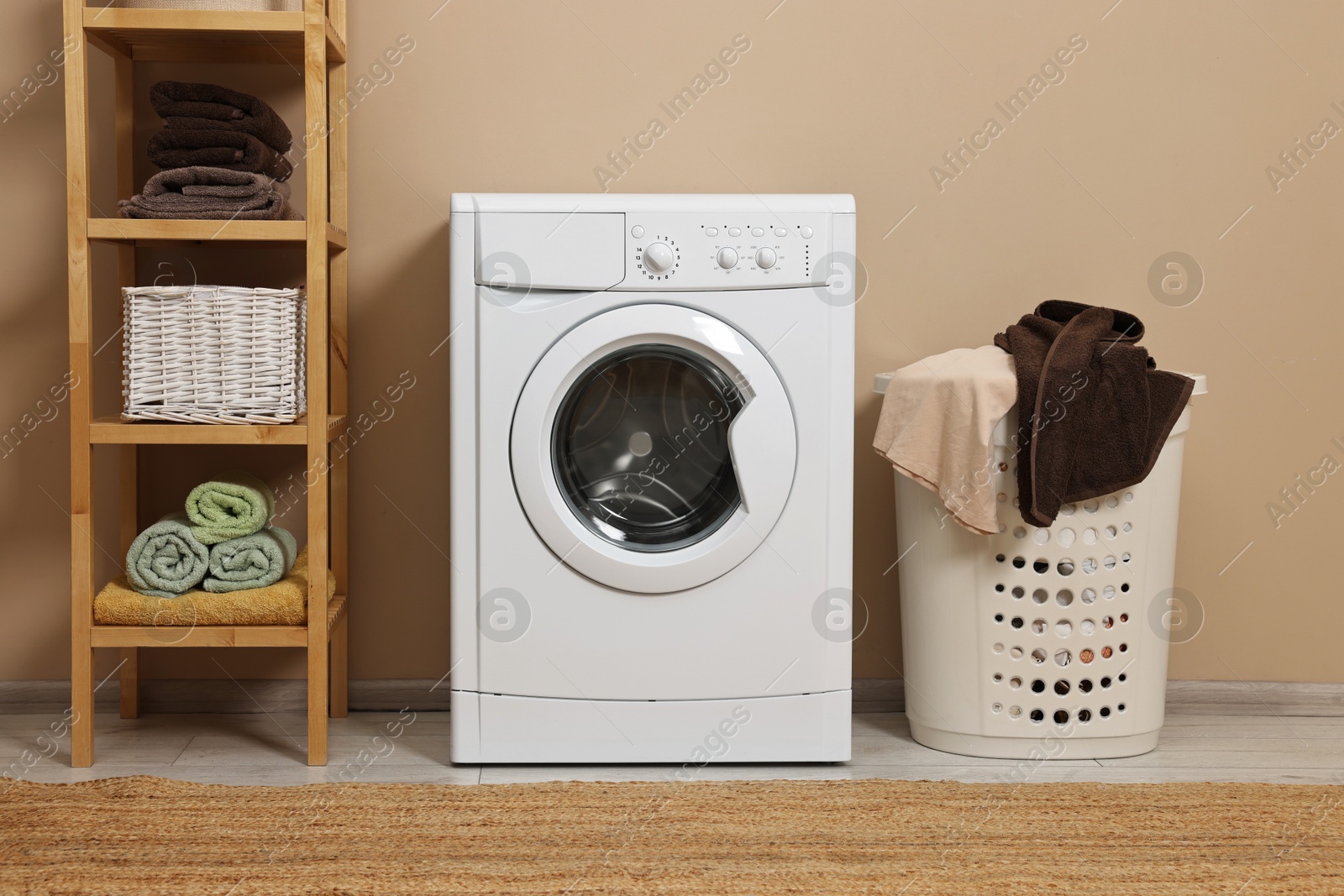 Photo of Washing machine, basket and shelving unit near beige wall indoors