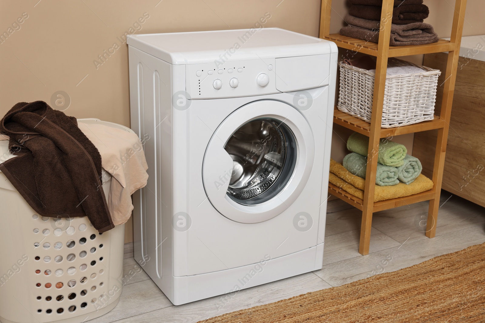 Photo of Washing machine, basket and shelving unit near beige wall indoors