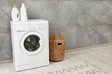 Photo of Washing machine, detergents, basket and rug in laundry room, space for text