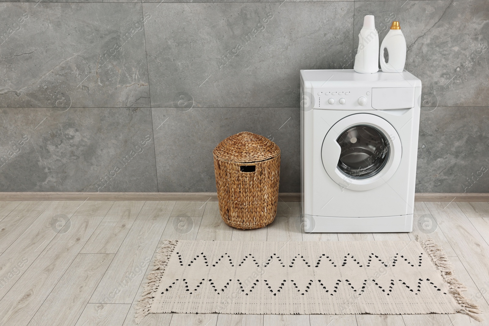 Photo of Washing machine, detergents, basket and rug in laundry room, space for text