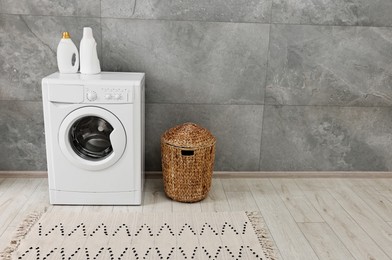 Photo of Washing machine, detergents, basket and rug in laundry room, space for text