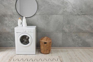 Photo of Washing machine, detergents, basket and mirror in laundry room, space for text