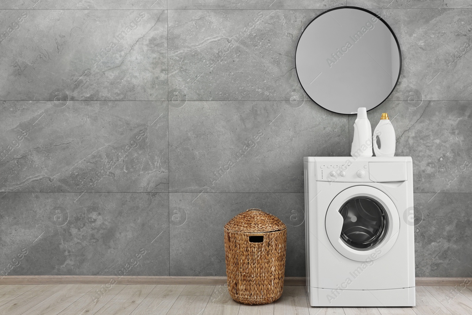 Photo of Washing machine, detergents, basket and mirror in laundry room, space for text