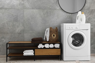 Photo of Washing machine, detergents, towels, basket and storage cabinet in laundry room