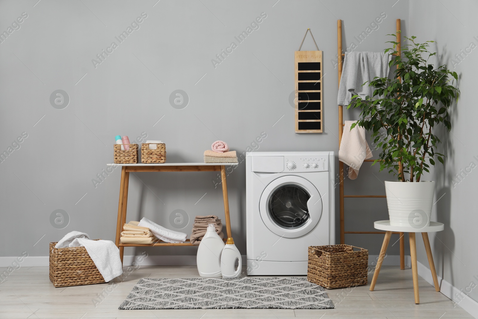 Photo of Washing machine, storage bench, detergents, laundry and houseplant indoors