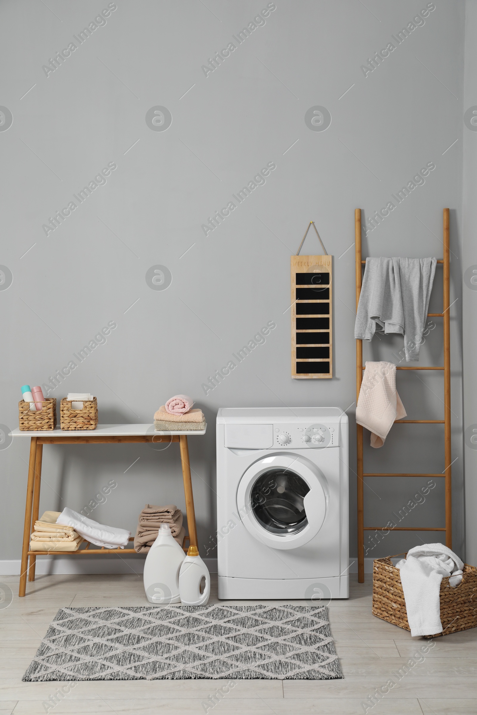 Photo of Washing machine, ladder, detergents, basket, laundry and storage bench indoors