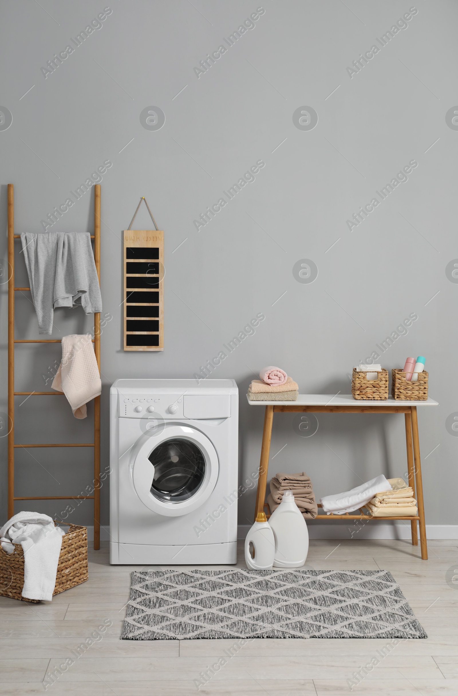 Photo of Washing machine, ladder, detergents, basket, laundry and storage bench indoors