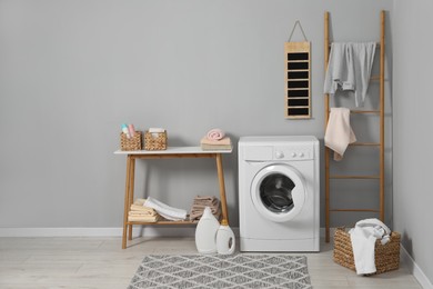 Photo of Washing machine, ladder, detergents, basket, laundry and storage bench indoors