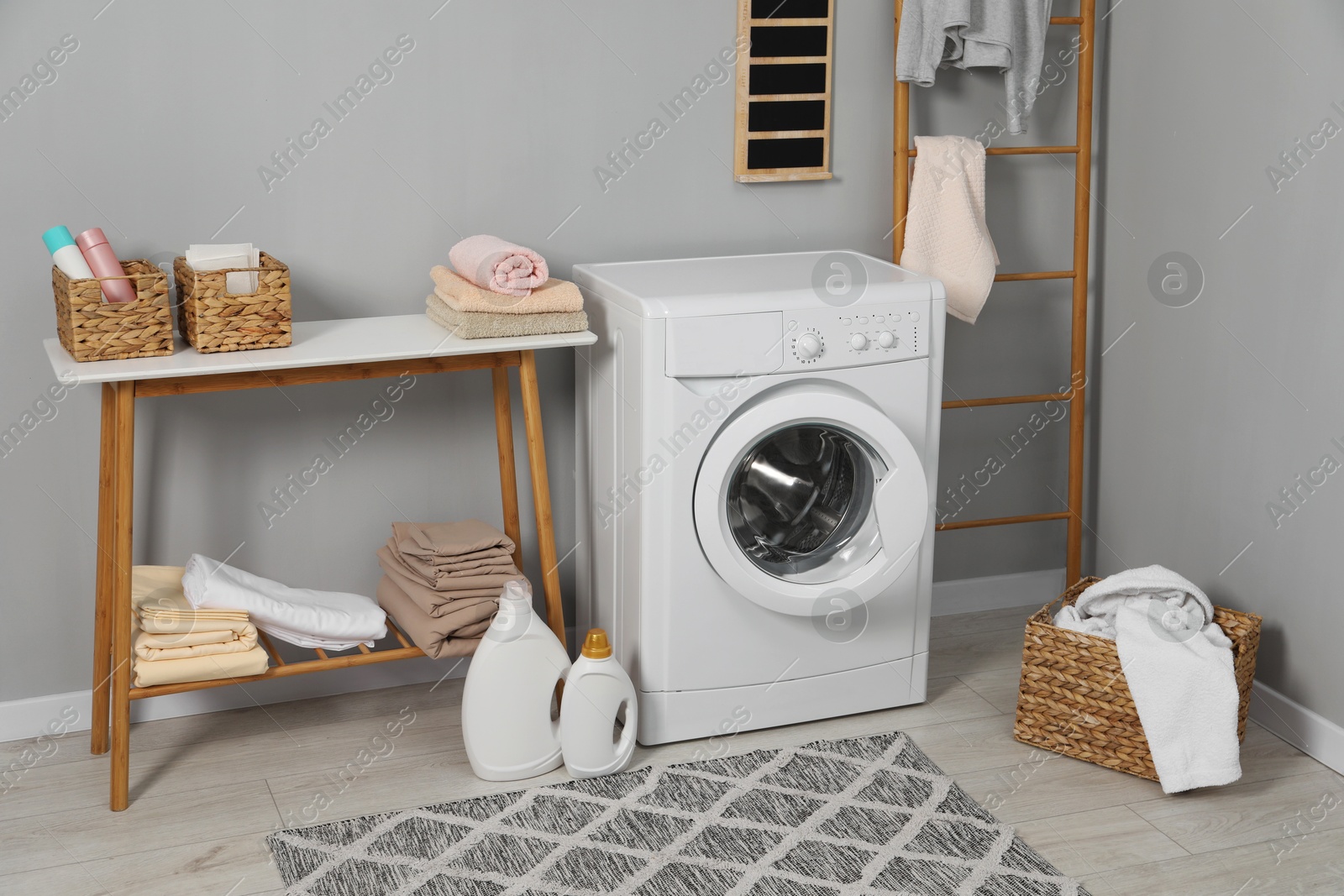 Photo of Washing machine, ladder, detergents, basket, laundry and storage bench indoors