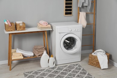 Photo of Washing machine, ladder, detergents, basket, laundry and storage bench indoors