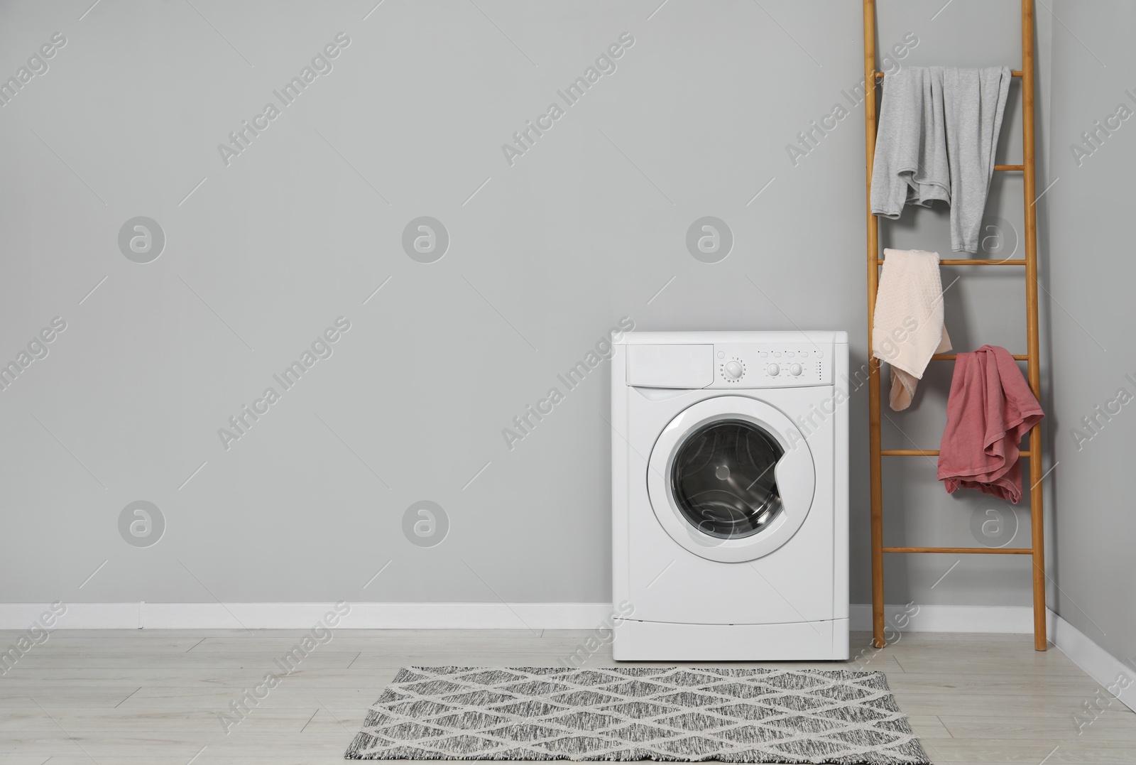 Photo of Washing machine, ladder and laundry near grey wall indoors, space for text