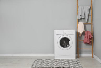 Photo of Washing machine, ladder and laundry near grey wall indoors, space for text