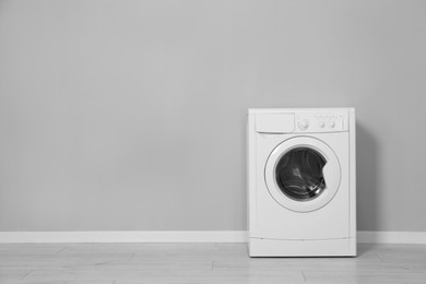 Washing machine near grey wall indoors, space for text