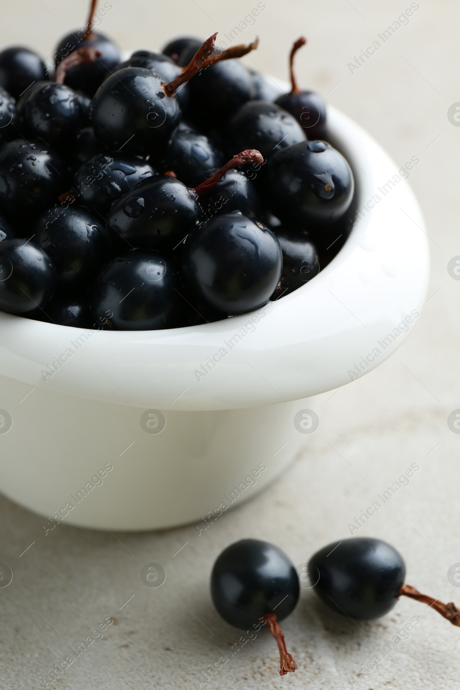 Photo of Ripe black currants in bowl on light table, closeup