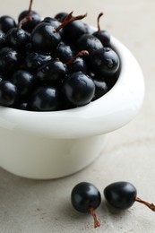 Photo of Ripe black currants in bowl on light table, closeup