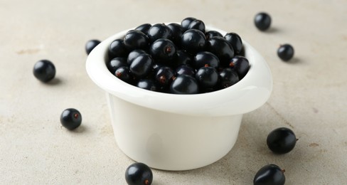 Ripe black currants in bowl on light table, closeup