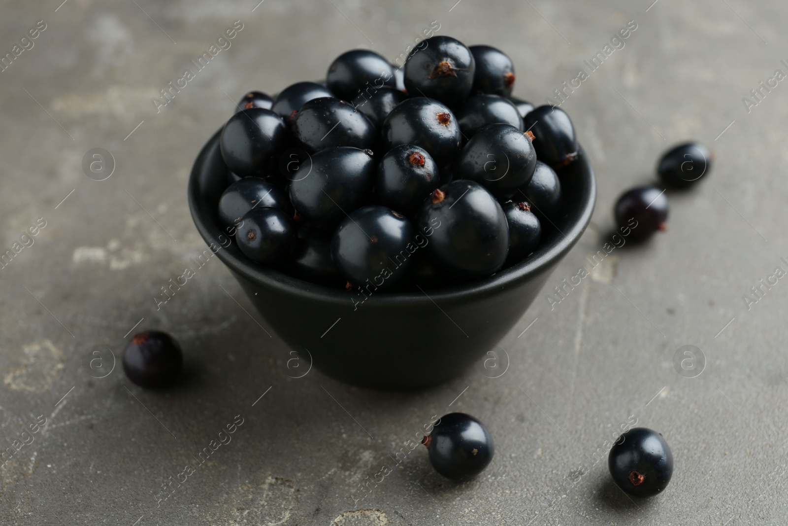 Photo of Ripe black currants in bowl on grey table