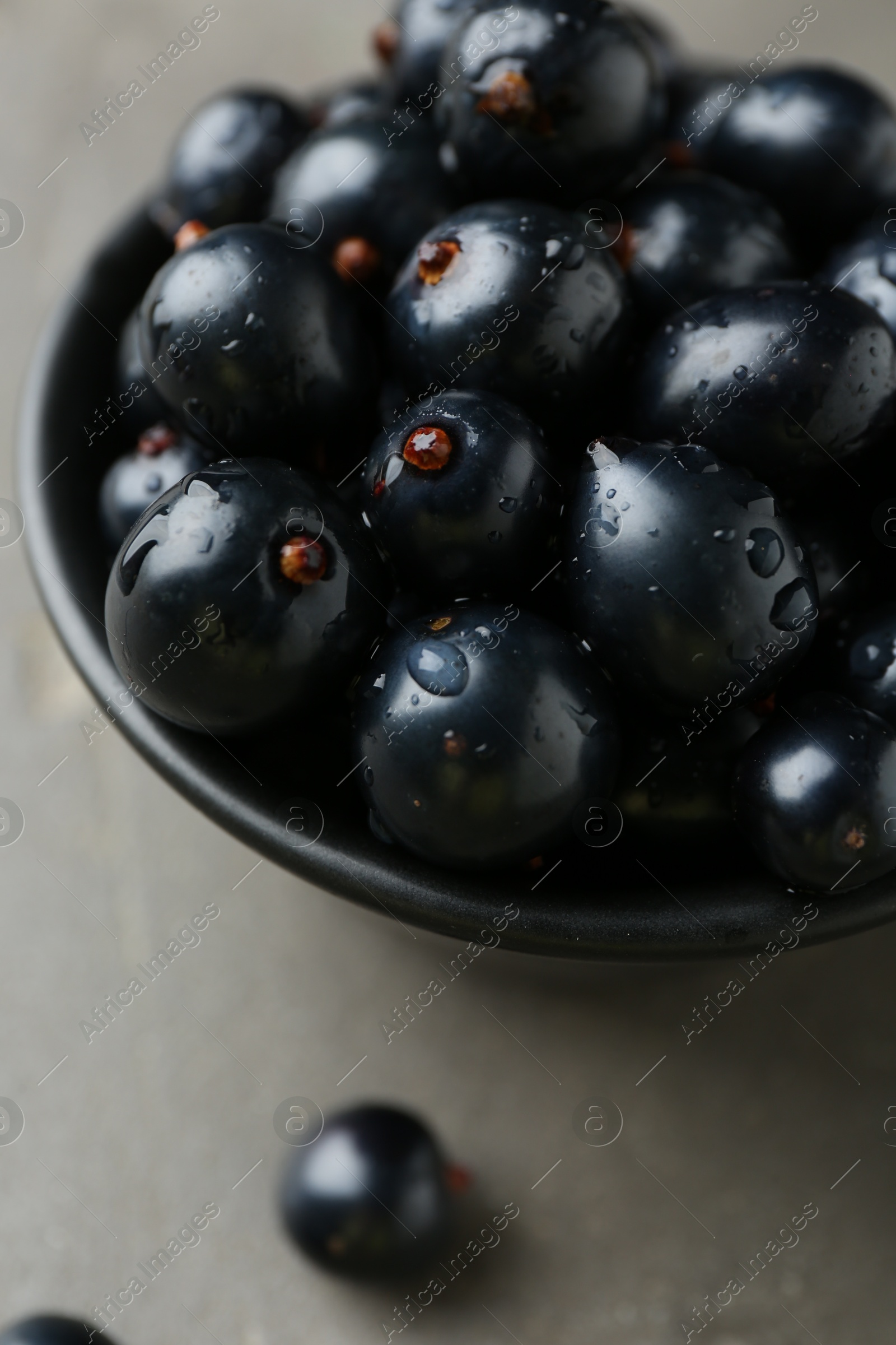 Photo of Ripe black currants in bowl on grey table, closeup