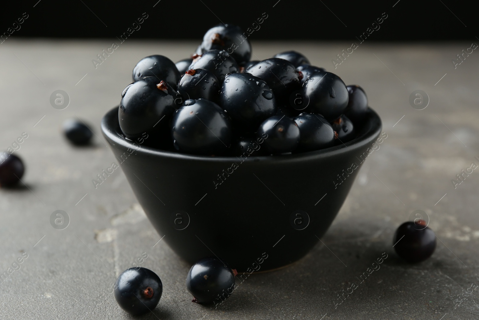 Photo of Ripe black currants in bowl on grey table, closeup