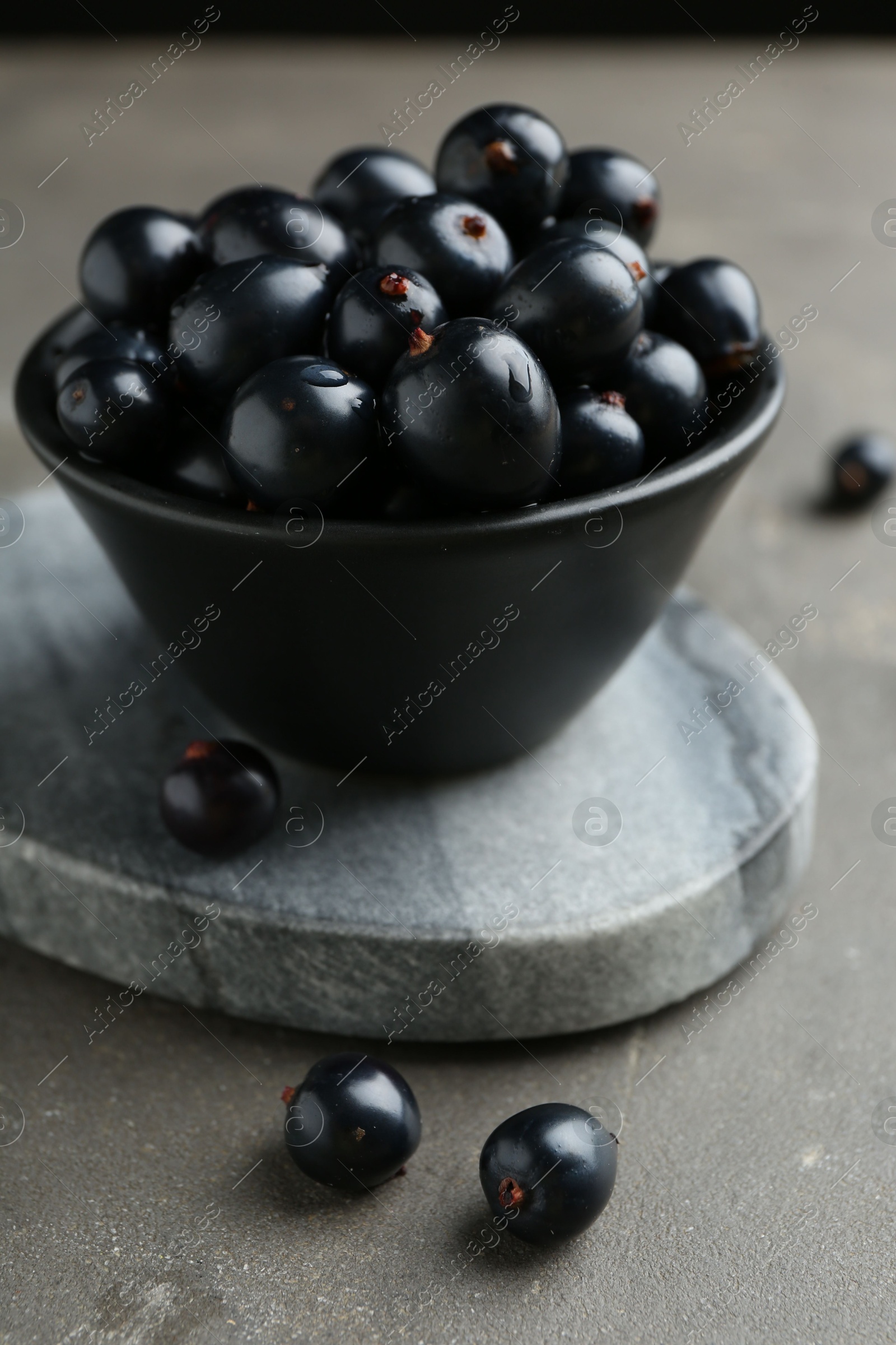 Photo of Ripe black currants in bowl on grey table