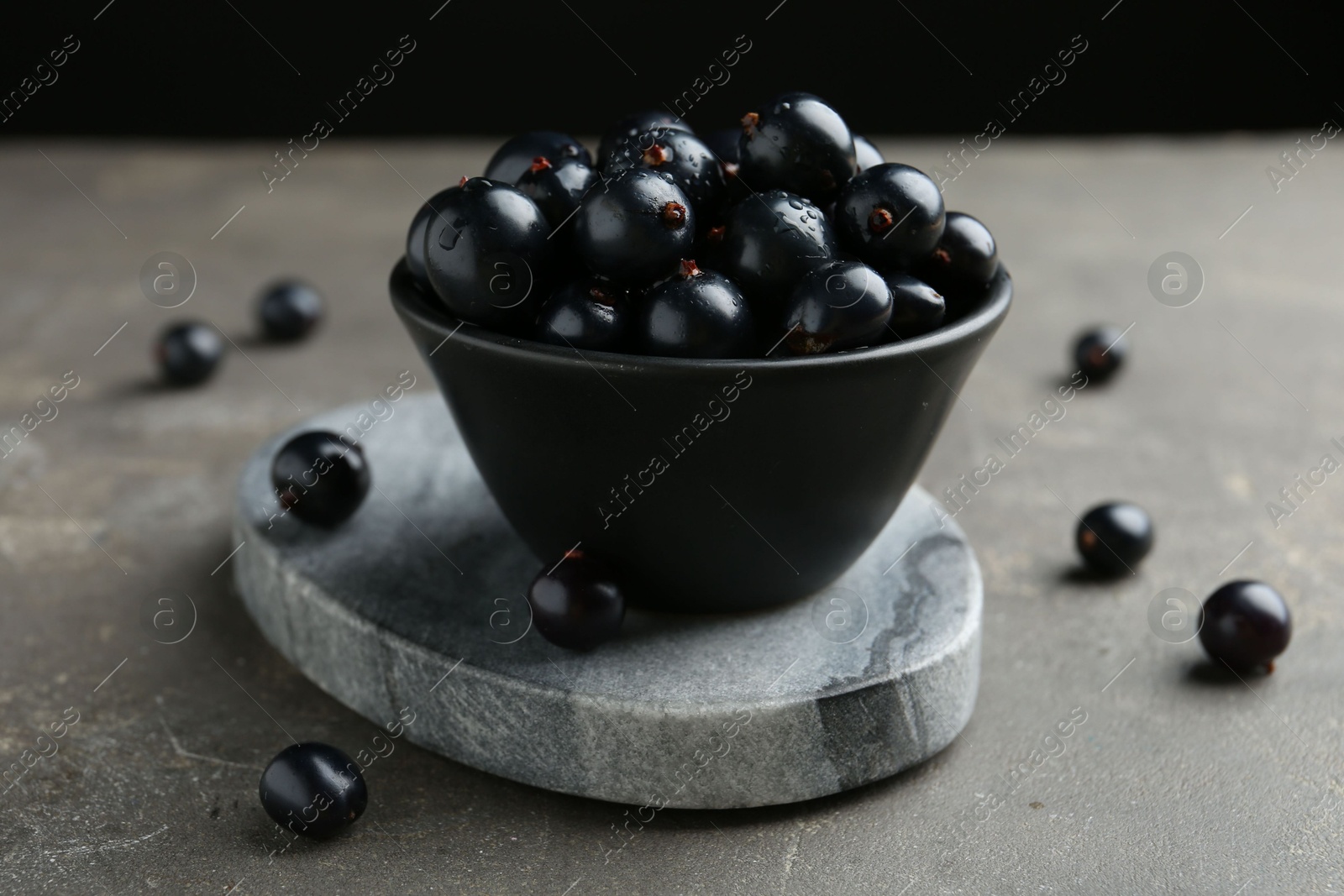 Photo of Ripe black currants in bowl on grey table, closeup