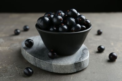 Photo of Ripe black currants in bowl on grey table, closeup