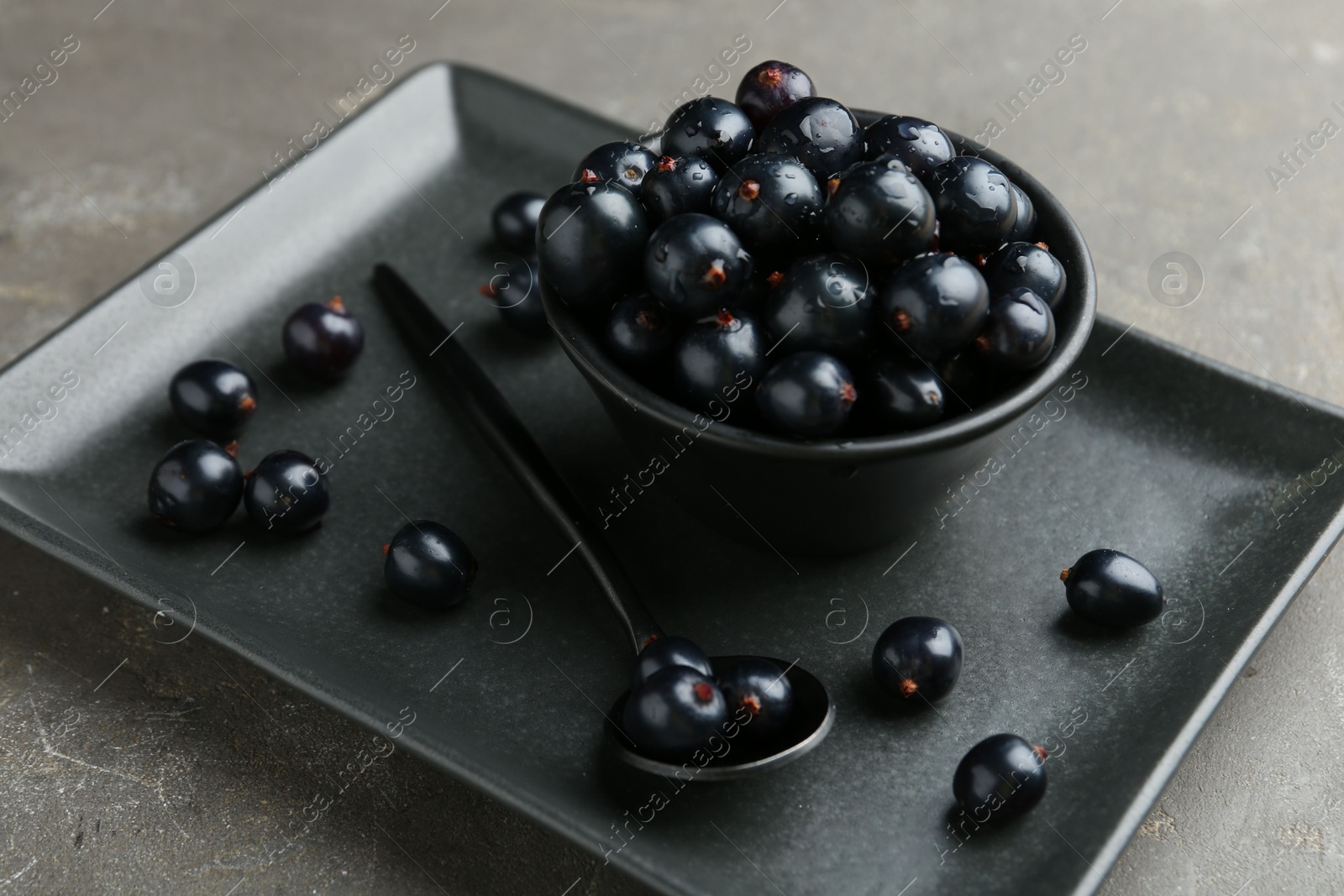 Photo of Ripe black currants with water drops on grey table