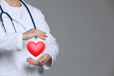 Image of Doctor holding red heart on grey background, closeup. Space for text