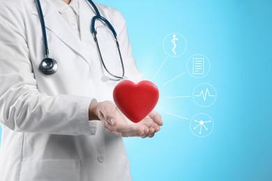 Image of Doctor holding red heart on light blue background, closeup. Icons near hands