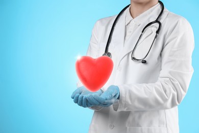 Image of Doctor holding red heart on light blue background, closeup. Space for text