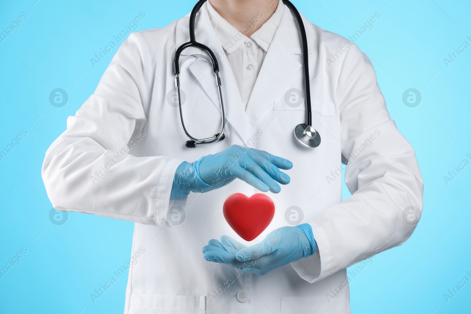 Image of Doctor holding red heart on light blue background, closeup