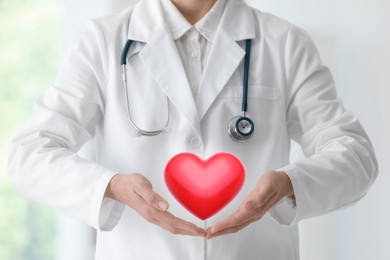 Image of Doctor holding red heart on blurred background, closeup