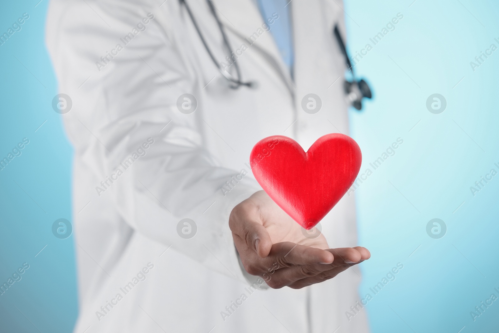 Image of Doctor holding red heart on light blue background, closeup