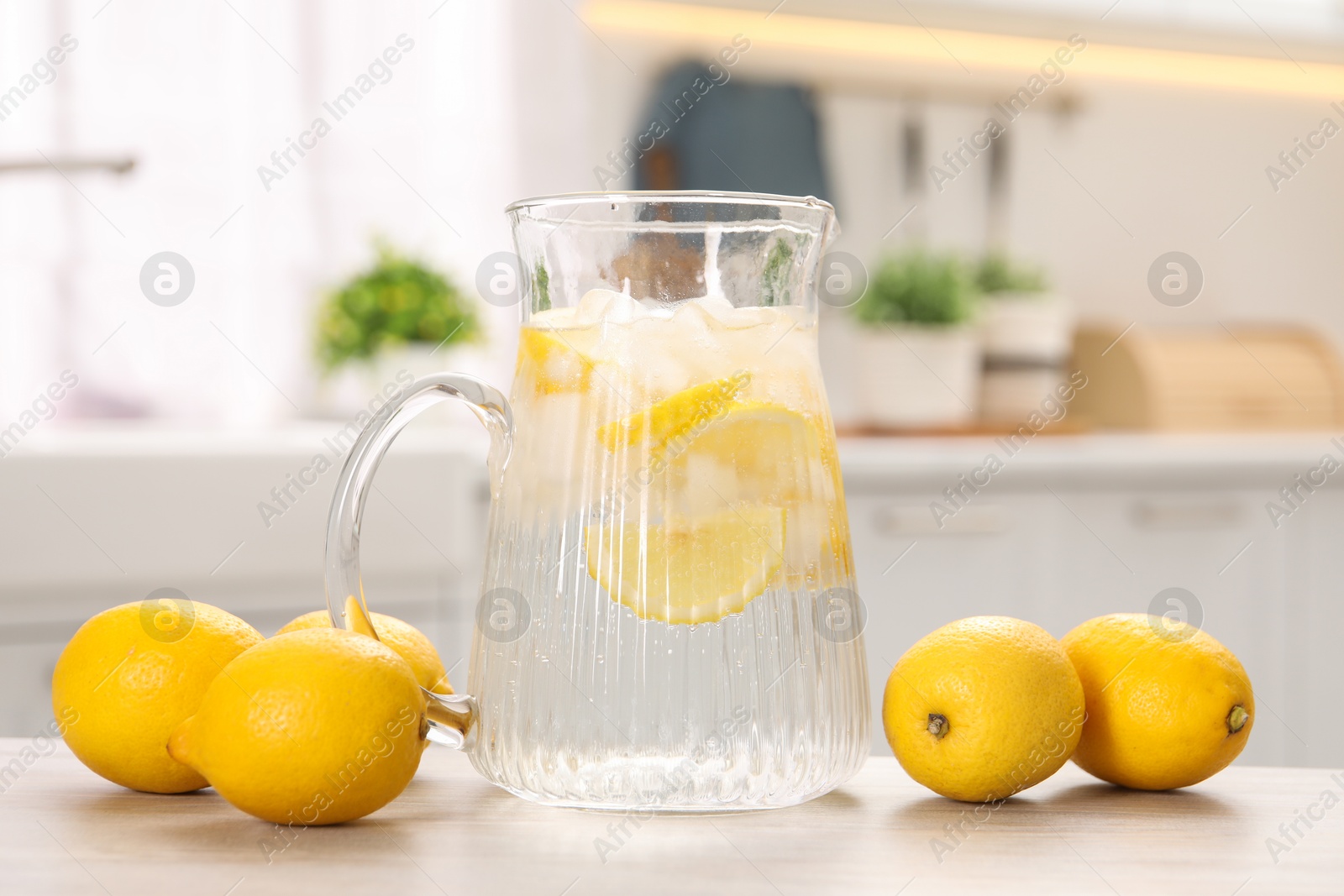 Photo of Freshly made lemonade in jug on white wooden table indoors