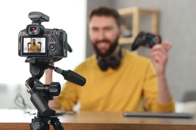 Photo of Technology blogger explaining something while recording video at home, focus on camera