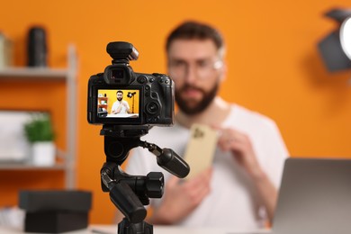 Photo of Technology blogger explaining something while recording video at home, focus on camera