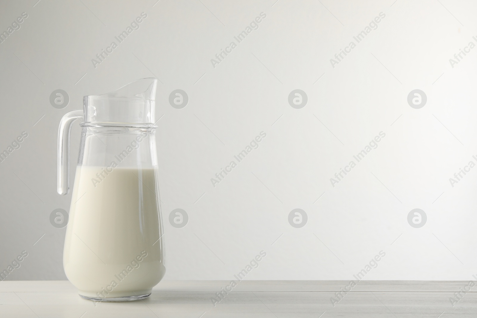 Photo of Glass jug with fresh milk on light wooden table. Space for text