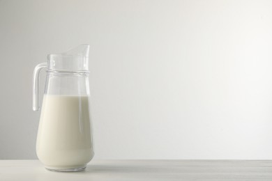 Photo of Glass jug with fresh milk on light wooden table. Space for text