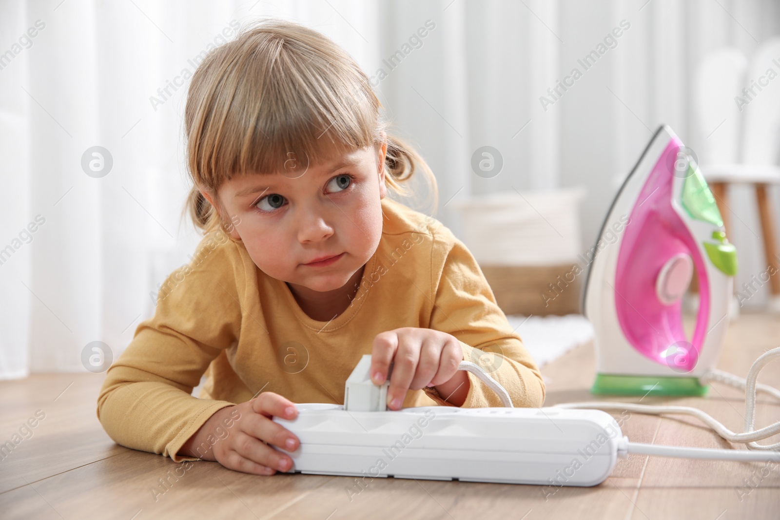 Photo of Little child playing with power strip and iron plug on floor indoors. Dangerous situation