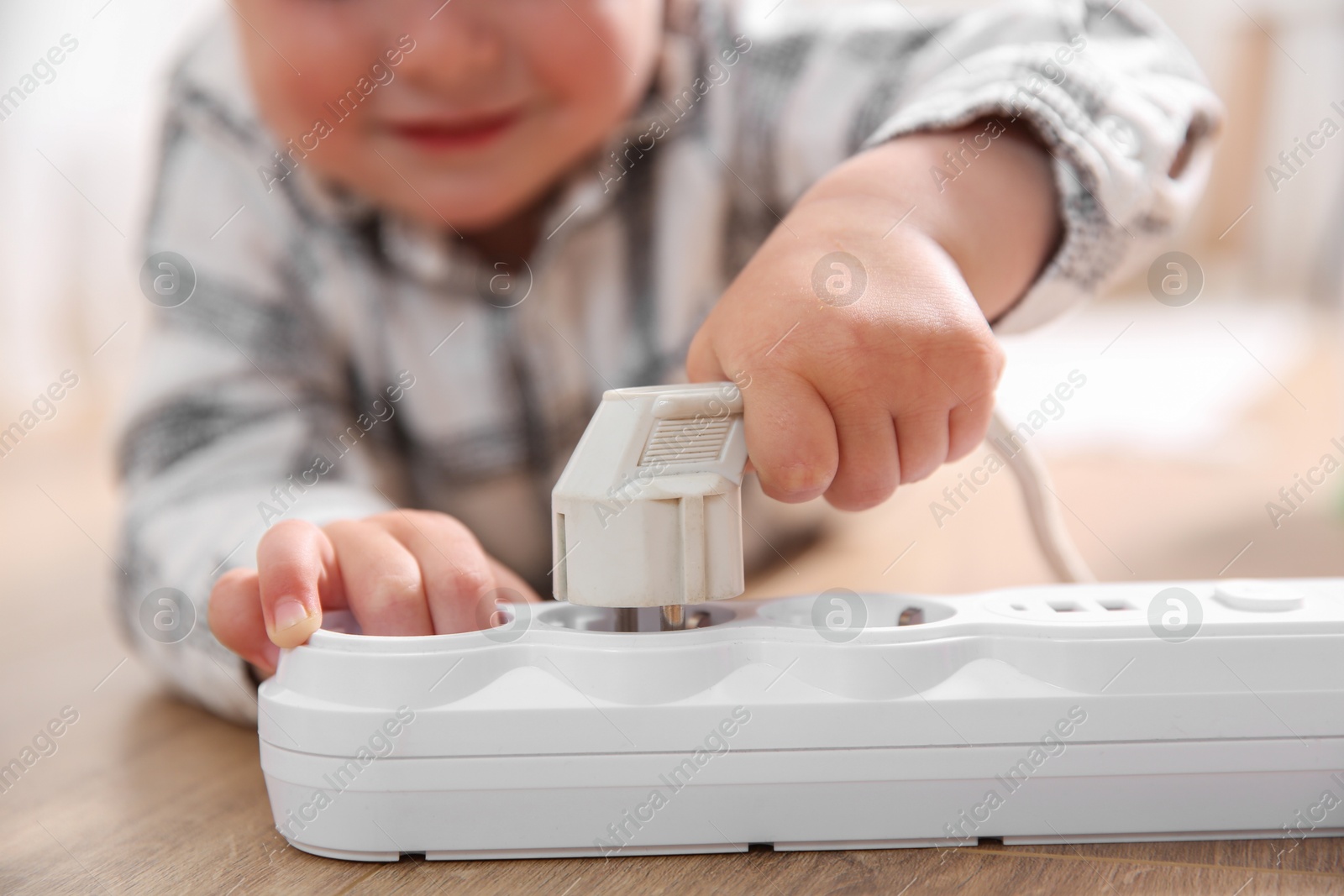 Photo of Little child playing with power strip and plug on floor indoors, closeup. Dangerous situation