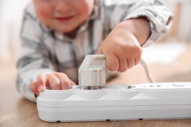 Little child playing with power strip and plug on floor indoors, closeup. Dangerous situation