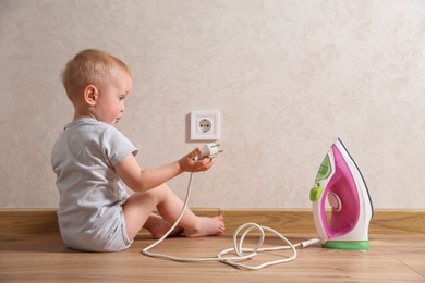 Photo of Little child playing with electrical socket and iron plug indoors. Dangerous situation