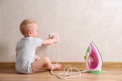 Photo of Little child playing with electrical socket and iron plug indoors. Dangerous situation