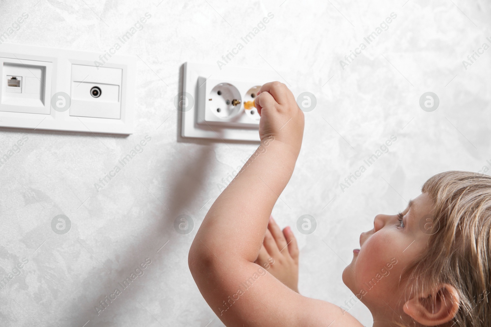 Photo of Little child playing with toy screwdriver and electrical socket at home, closeup. Dangerous situation