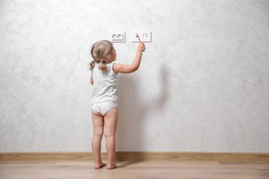 Photo of Little child playing with electrical socket and pencil indoors. Dangerous situation