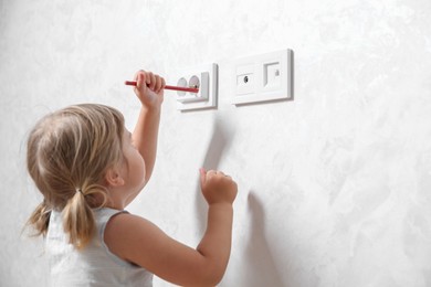 Photo of Little child playing with electrical socket and pencil indoors, space for text. Dangerous situation