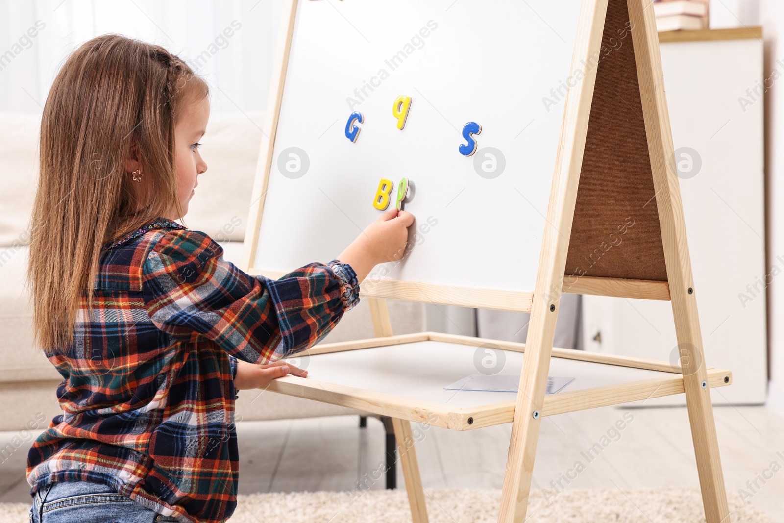 Photo of Cute little girl putting magnetic letters on board at home. Learning alphabet