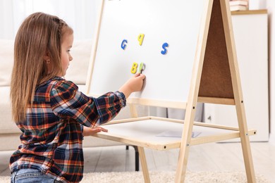 Photo of Cute little girl putting magnetic letters on board at home. Learning alphabet