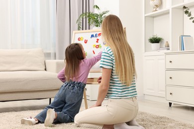 Photo of Mom teaching her daughter alphabet with magnetic letters at home